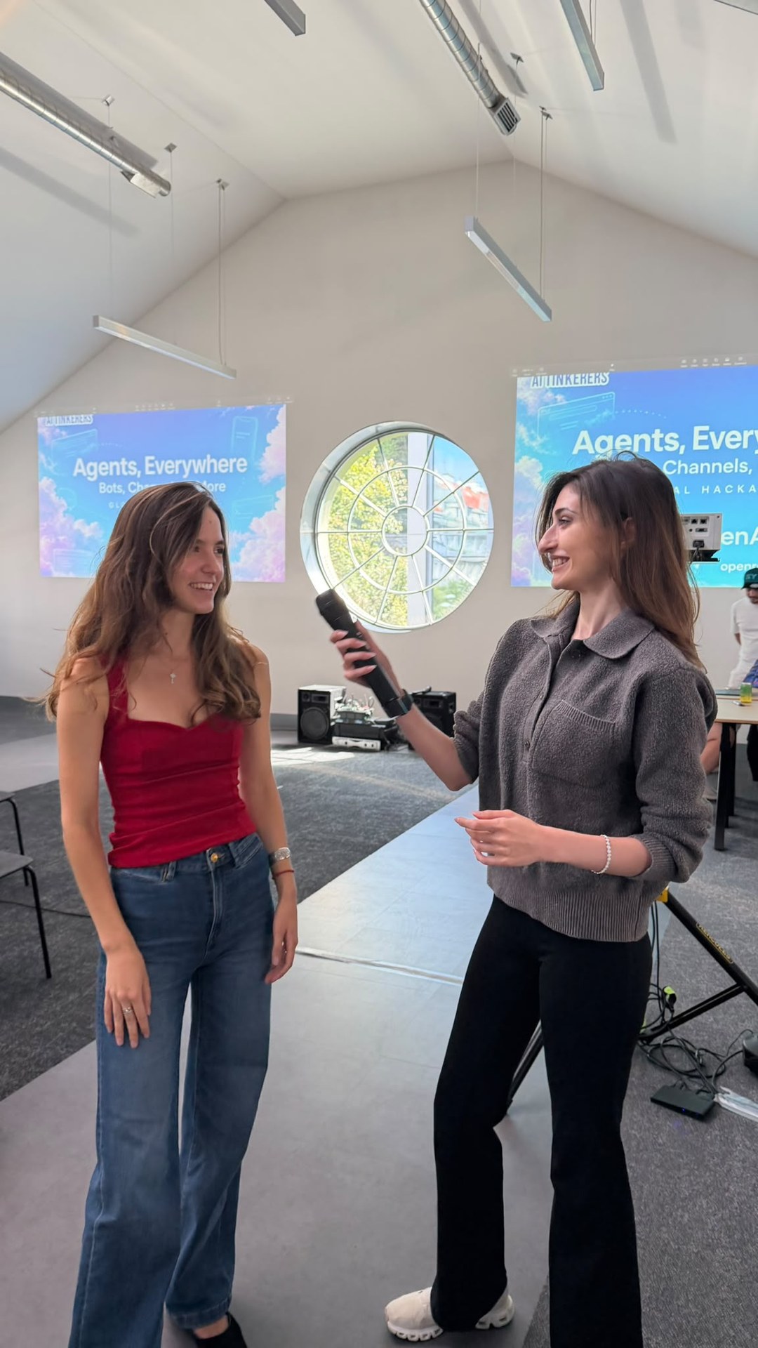 Sofie and a fellow host sharing a microphone at the Agents, Everywhere global hackathon with OpenAI